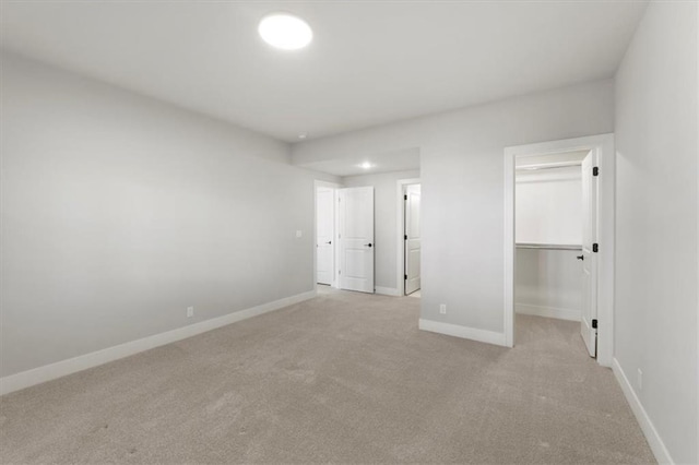 unfurnished bedroom with a walk in closet, a closet, light carpet, and baseboards