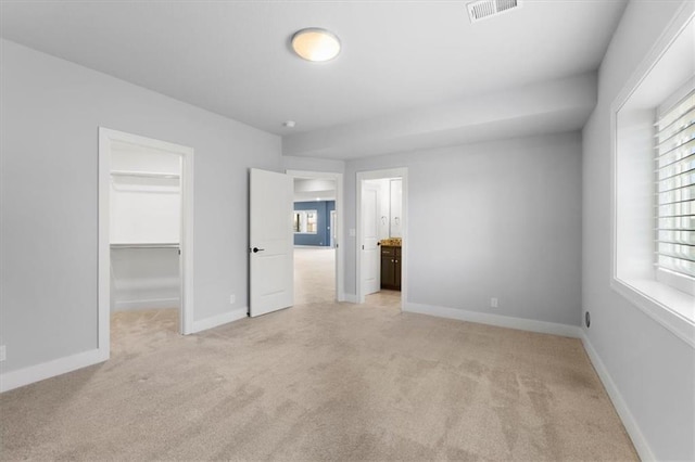 unfurnished bedroom featuring visible vents, baseboards, light colored carpet, a walk in closet, and a closet