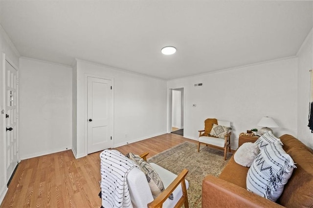 living area with baseboards, visible vents, light wood-style flooring, and crown molding