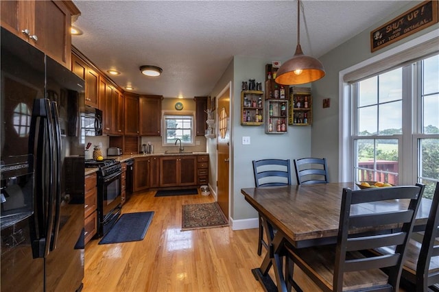 kitchen featuring light countertops, hanging light fixtures, light wood-style floors, a textured ceiling, and black appliances