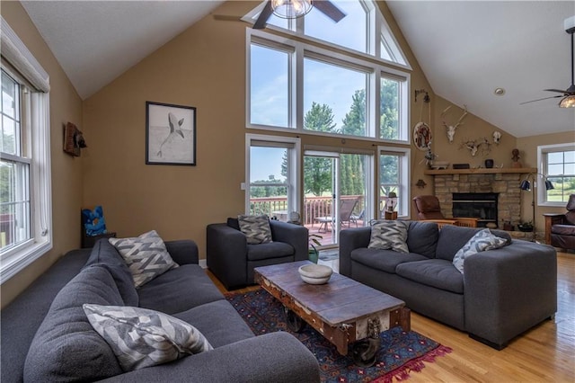 living area featuring light wood finished floors, high vaulted ceiling, a stone fireplace, and a ceiling fan