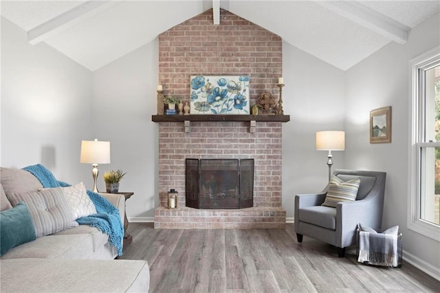 living area featuring lofted ceiling with beams, a brick fireplace, wood finished floors, and baseboards