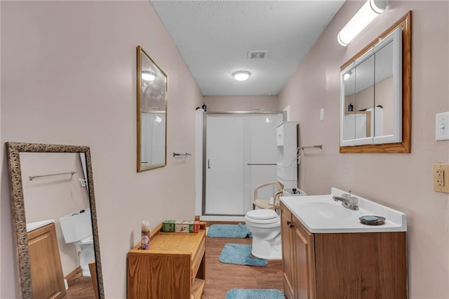 bathroom featuring toilet, wood finished floors, visible vents, vanity, and a shower stall