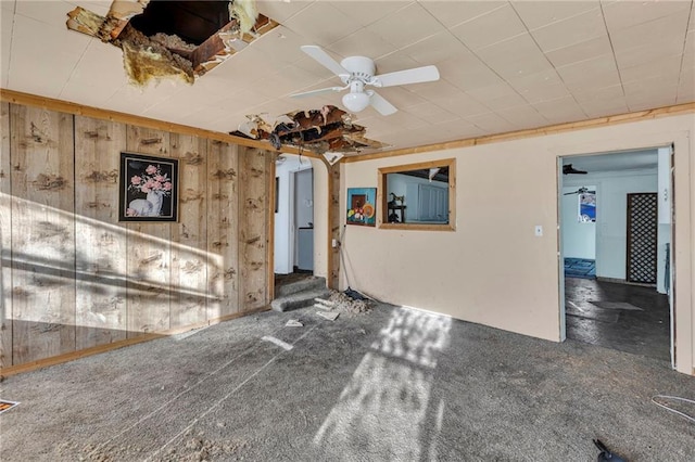 interior space featuring a ceiling fan, wood walls, and carpet floors