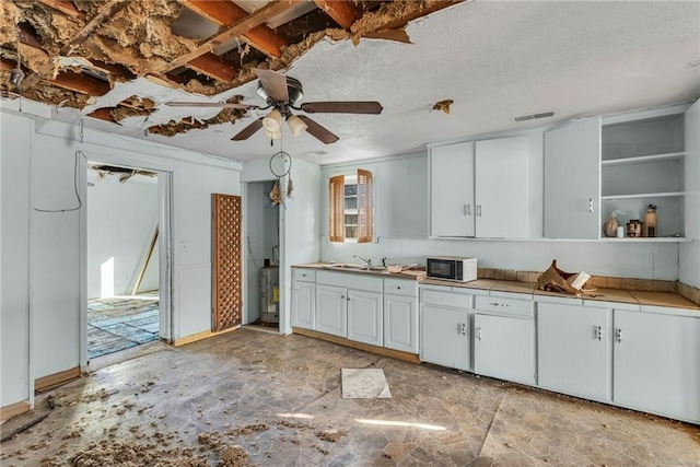 kitchen with black microwave, tile counters, a textured ceiling, white cabinetry, and a sink