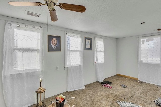 foyer entrance featuring a ceiling fan, visible vents, a textured ceiling, and carpet flooring