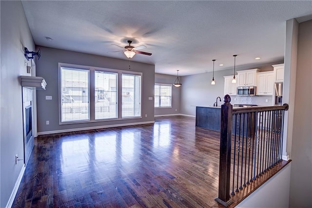 living room featuring baseboards, a textured ceiling, dark wood finished floors, and a ceiling fan