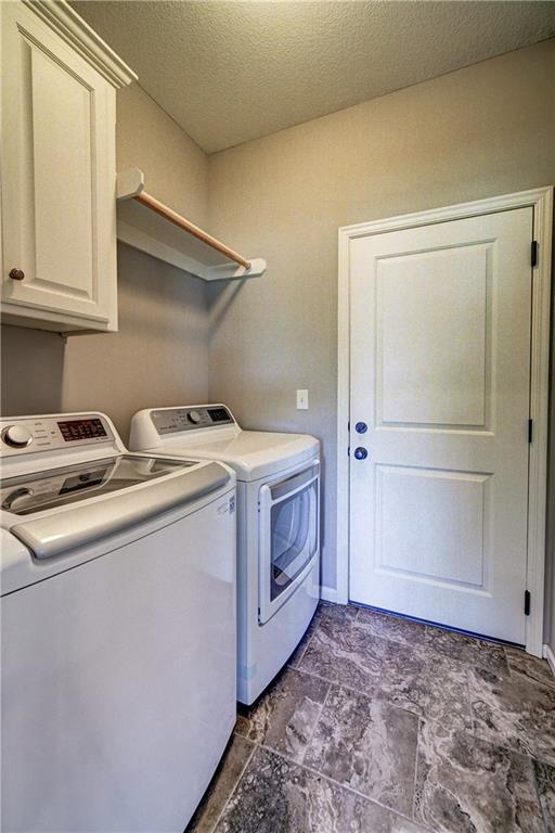 clothes washing area featuring washer and clothes dryer, cabinet space, and a textured ceiling