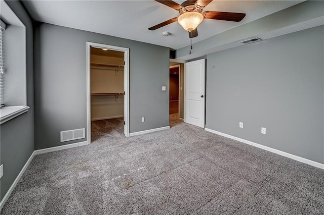 unfurnished bedroom with a walk in closet, carpet flooring, baseboards, and visible vents