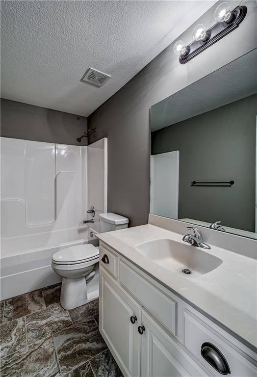 bathroom with visible vents, toilet, bathing tub / shower combination, a textured ceiling, and vanity