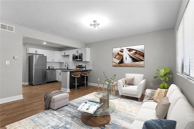 living room featuring baseboards, a textured ceiling, visible vents, and wood finished floors