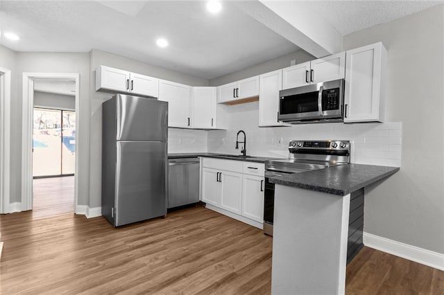 kitchen featuring stainless steel appliances, dark countertops, light wood-style floors, white cabinets, and a peninsula