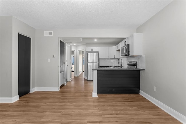 kitchen featuring stainless steel appliances, dark countertops, visible vents, light wood-style floors, and white cabinets