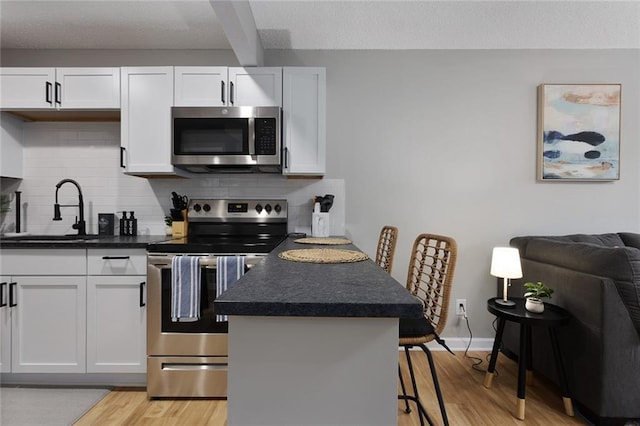 kitchen with stainless steel appliances, dark countertops, decorative backsplash, a sink, and light wood-type flooring