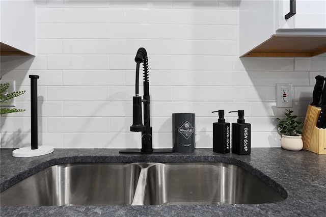 details with backsplash, dark stone countertops, a sink, and white cabinetry