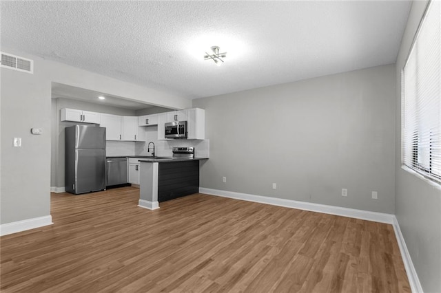 kitchen with visible vents, dark countertops, open floor plan, stainless steel appliances, and light wood-style floors