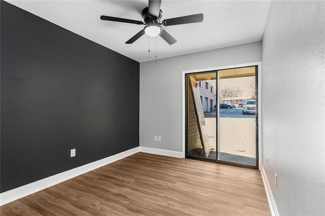 empty room featuring a textured ceiling, ceiling fan, wood finished floors, and baseboards