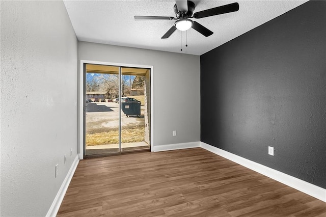 empty room with a textured ceiling, baseboards, wood finished floors, and a textured wall