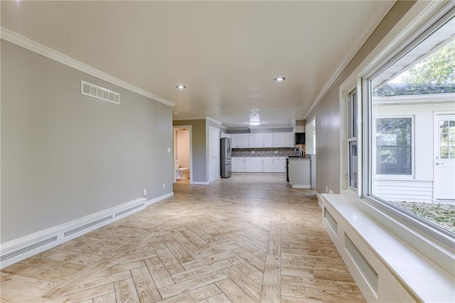 unfurnished living room with a baseboard radiator, visible vents, a wealth of natural light, and ornamental molding