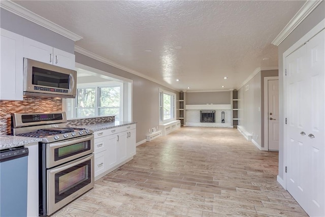 kitchen featuring stainless steel appliances, white cabinetry, a fireplace, and light wood finished floors