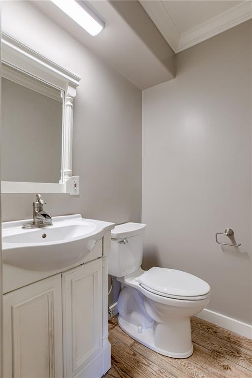 half bathroom with toilet, ornamental molding, vanity, wood finished floors, and baseboards