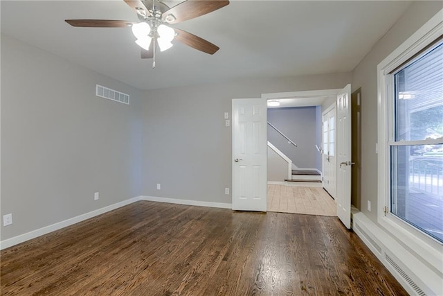 unfurnished room with dark wood-style floors, visible vents, ceiling fan, and baseboards