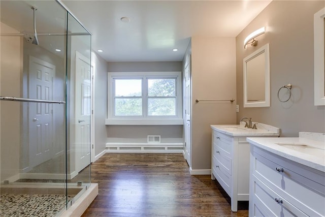 full bath with two vanities, a sink, a shower stall, wood finished floors, and baseboards