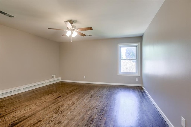 spare room featuring dark wood-type flooring, a ceiling fan, visible vents, and baseboards