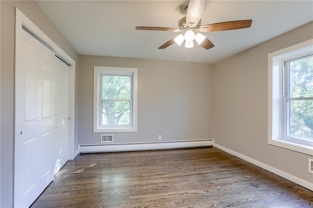 unfurnished bedroom with a closet, multiple windows, baseboard heating, and wood finished floors