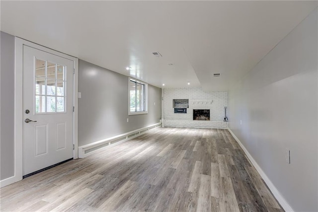 unfurnished living room featuring a brick fireplace, wood finished floors, visible vents, and baseboards