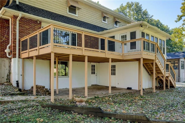 rear view of property with roof with shingles, a patio, brick siding, stairway, and a deck