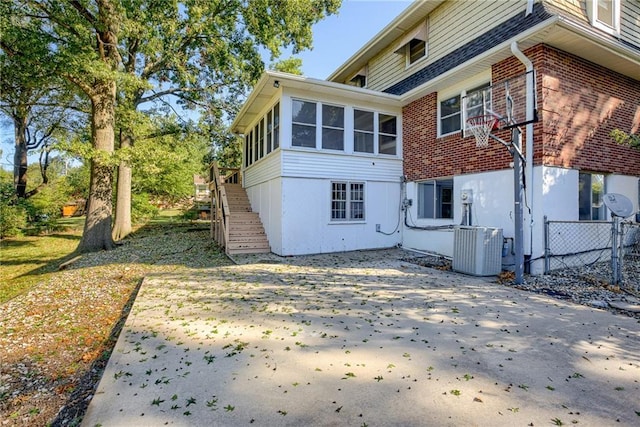 back of house with central AC unit, a sunroom, stairs, fence, and brick siding