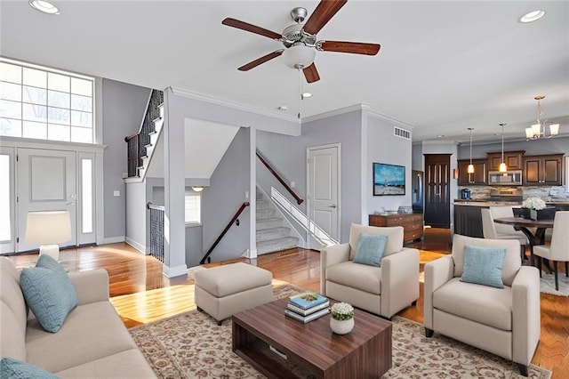 living room with light wood finished floors, baseboards, visible vents, ornamental molding, and stairs