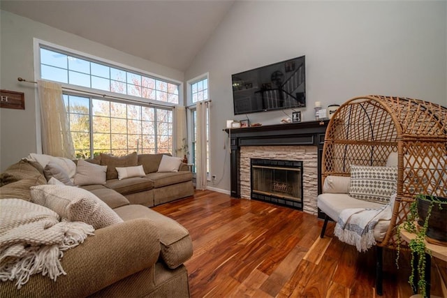 living area with baseboards, high vaulted ceiling, wood finished floors, and a stone fireplace