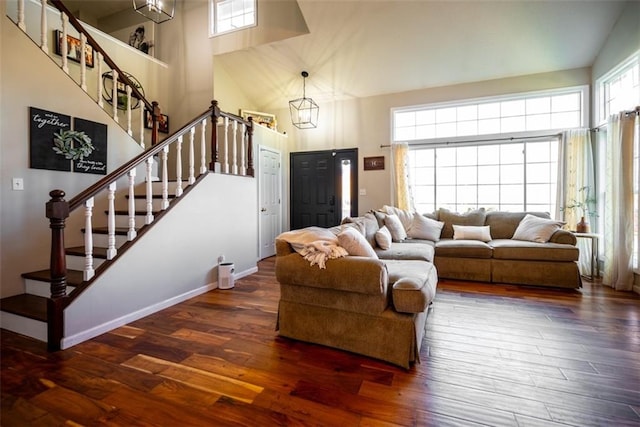 living area featuring a towering ceiling, wood finished floors, a chandelier, baseboards, and stairs