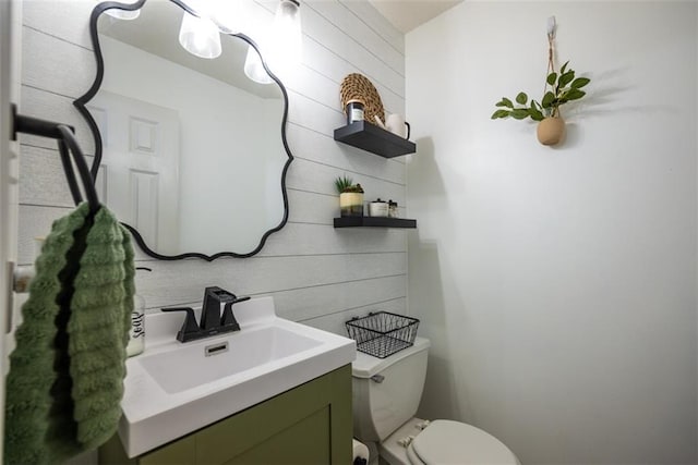 bathroom with toilet, wooden walls, and vanity