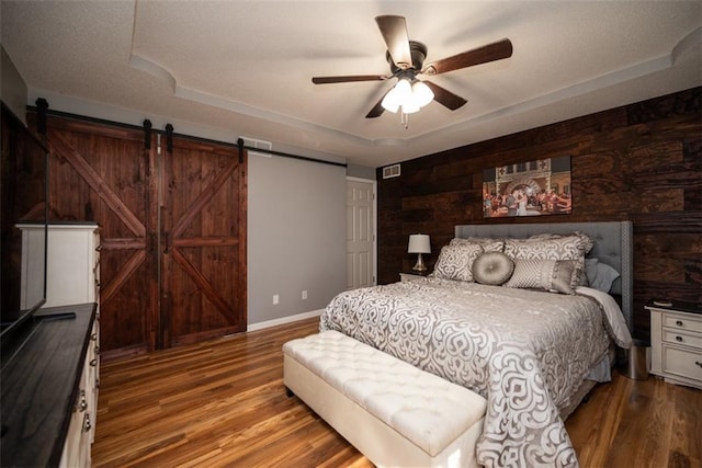 bedroom featuring a tray ceiling, a barn door, and wood finished floors