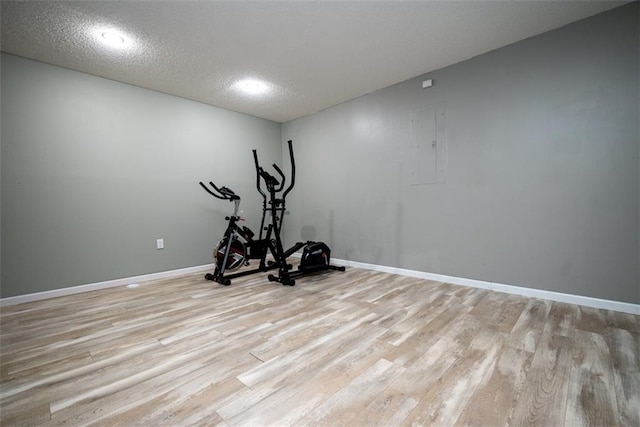 workout room with a textured ceiling, electric panel, light wood-style flooring, and baseboards