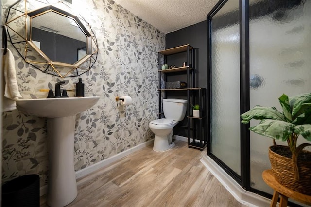 full bathroom featuring wallpapered walls, toilet, wood finished floors, a textured ceiling, and a shower stall