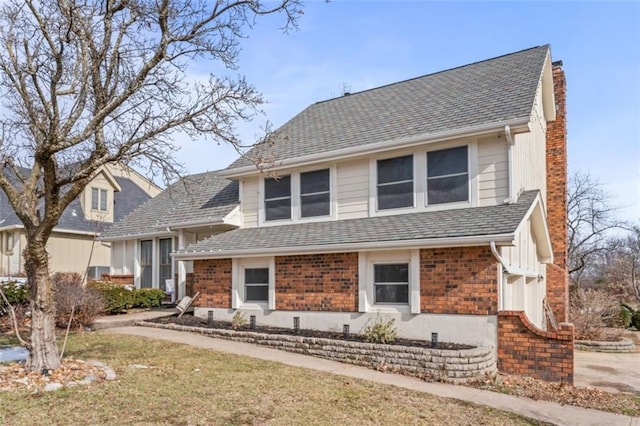 view of front of property with roof with shingles, a chimney, and brick siding