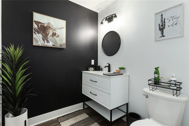 half bath featuring wood finished floors, vanity, toilet, and baseboards