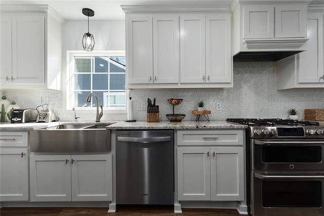 kitchen with light stone counters, stainless steel appliances, a sink, decorative backsplash, and decorative light fixtures