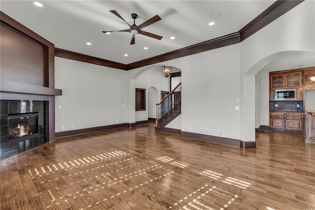 unfurnished living room featuring arched walkways, visible vents, stairway, a tile fireplace, and baseboards