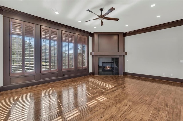 unfurnished living room featuring plenty of natural light, a fireplace, wood finished floors, and crown molding