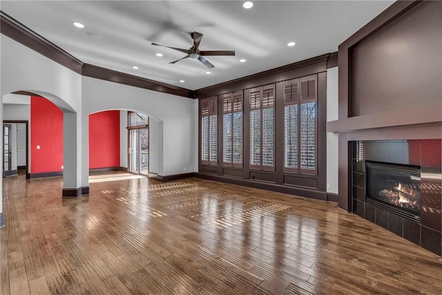 unfurnished living room with ornamental molding, arched walkways, baseboards, and wood finished floors