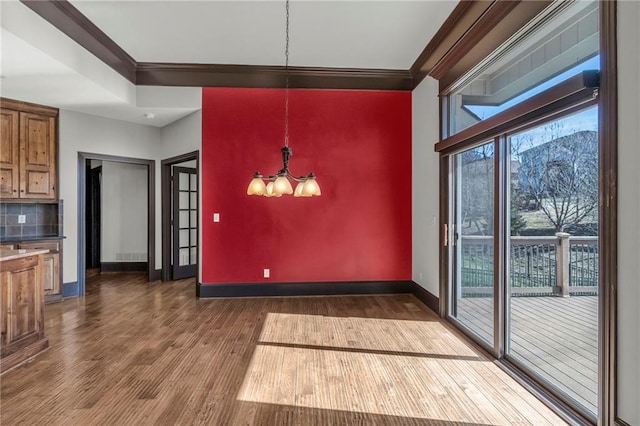 unfurnished dining area featuring a chandelier, crown molding, baseboards, and wood finished floors