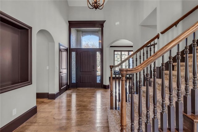 foyer featuring arched walkways, baseboards, a high ceiling, and hardwood / wood-style floors