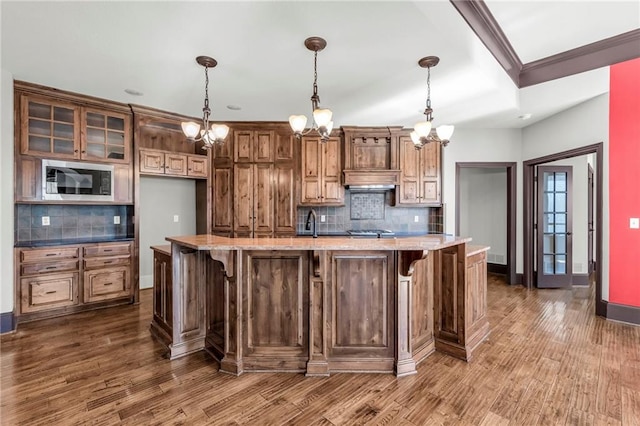 kitchen with a breakfast bar area, dark wood-style flooring, baseboards, stainless steel microwave, and glass insert cabinets