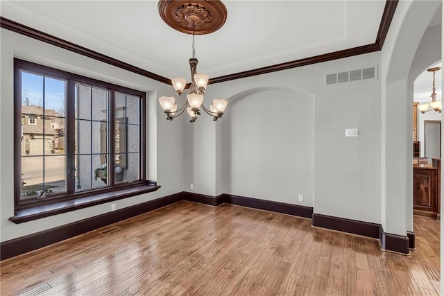 empty room featuring arched walkways, visible vents, light wood-style floors, ornamental molding, and an inviting chandelier