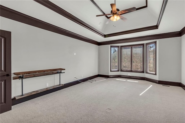 empty room with a ceiling fan, baseboards, a tray ceiling, carpet, and crown molding